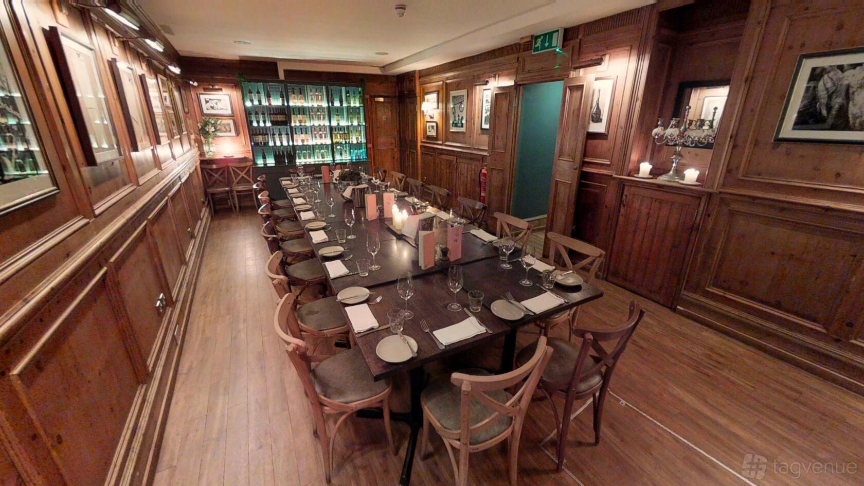 A dining room with long wooden tables, wine bottle display, and wood-paneled walls at Brasserie Blanc Chancery Lane.