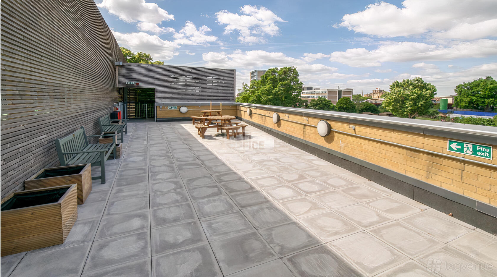 An outdoor terrace with wooden benches, picnic tables, and city views at Haileybury Sports and Events Centre.