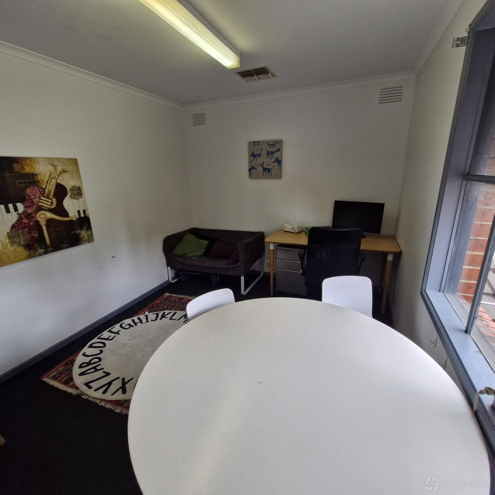 An office space with a round table, white chairs, a sofa, and a desk with a computer at Happy Hubbub.