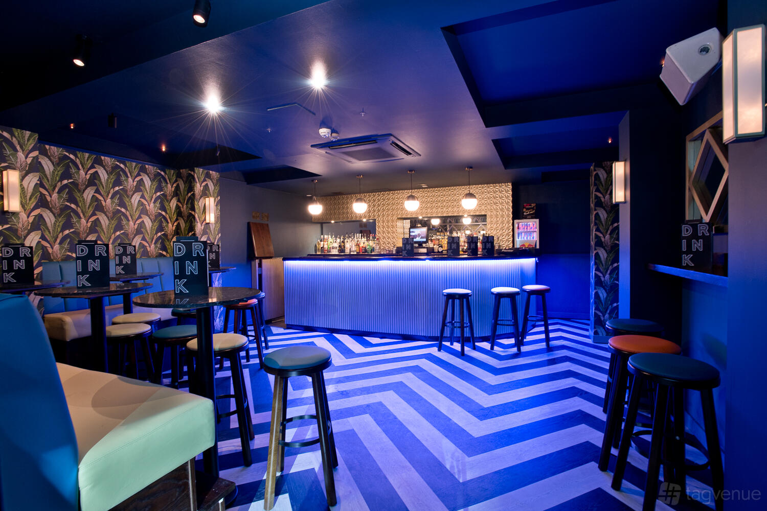 An event space in a bar with blue chevron floors, patterned wallpaper, and a lit counter at Sway.
