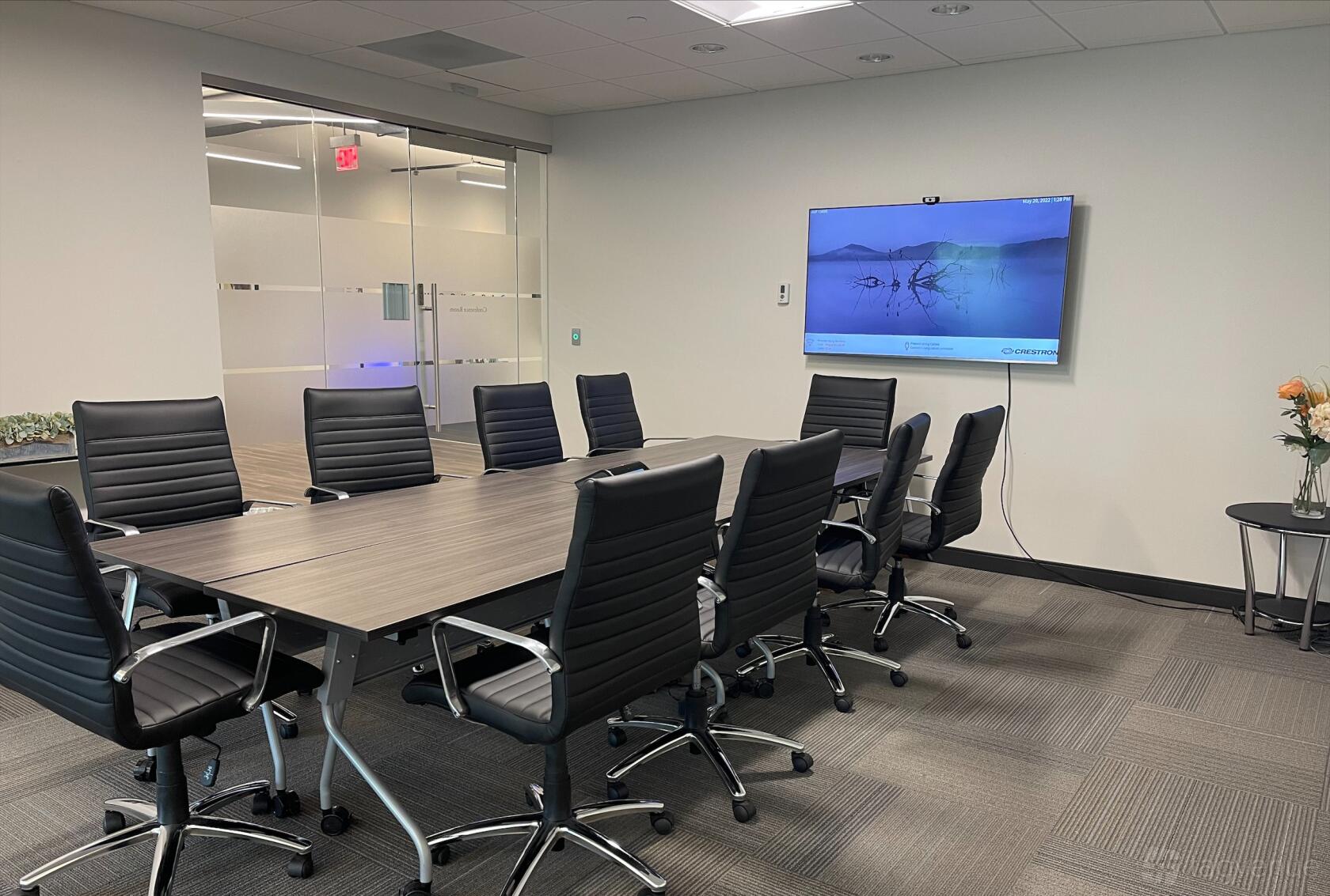 A meeting room with a long conference table, black leather chairs, and wall-mounted screen at Capital Workspaces Bethesda.