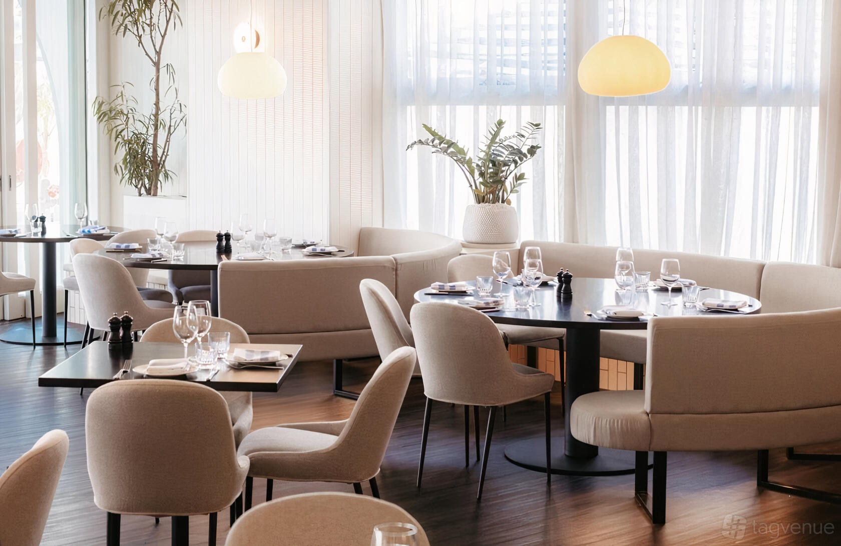 A restaurant with neutral-toned upholstered chairs, round tables set with glassware, and large windows at Fosh Portside.