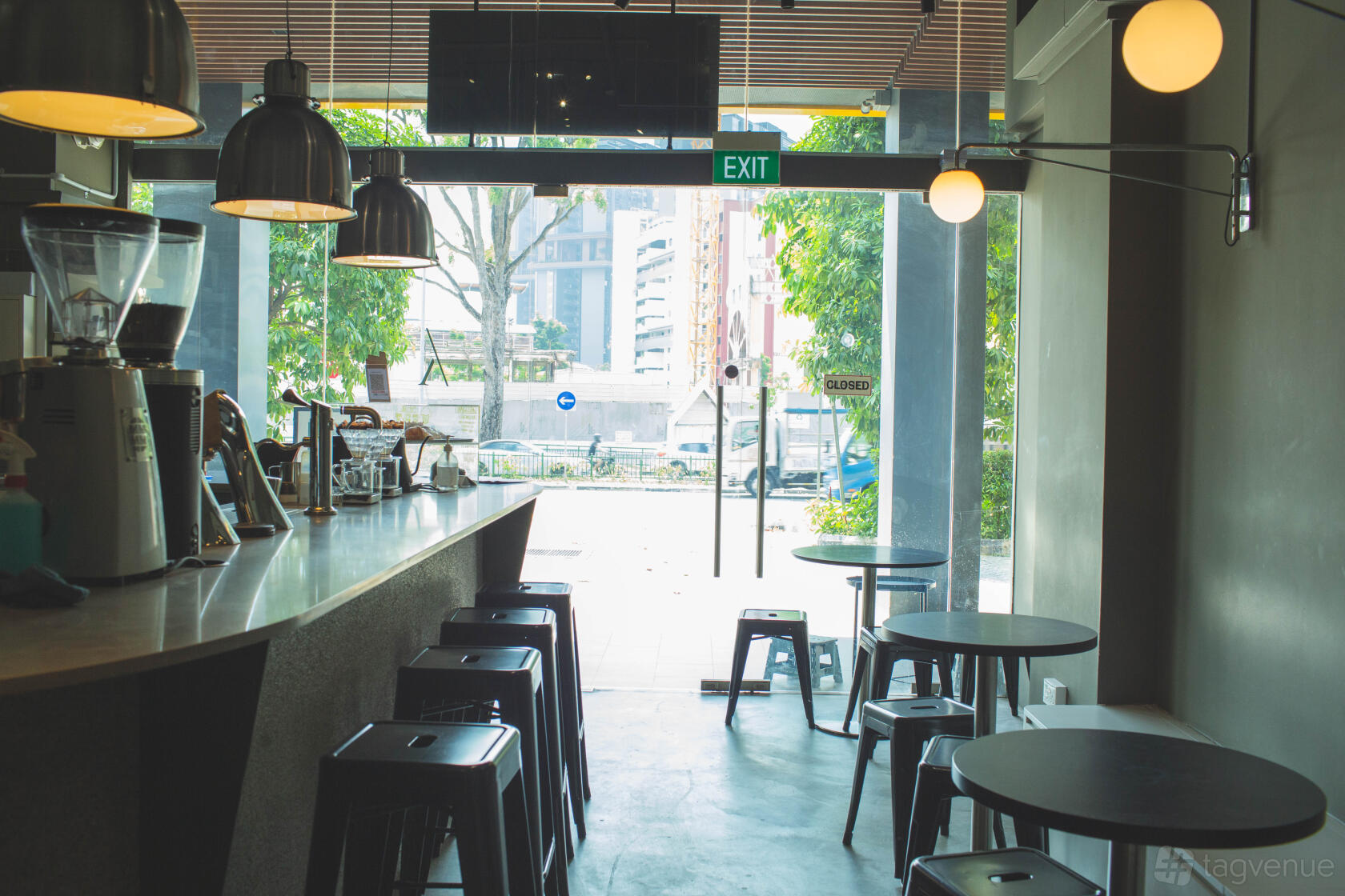 A cafe with floor-to-ceiling windows, round tables, black stools, and hanging pendant lights at State Of Affairs.