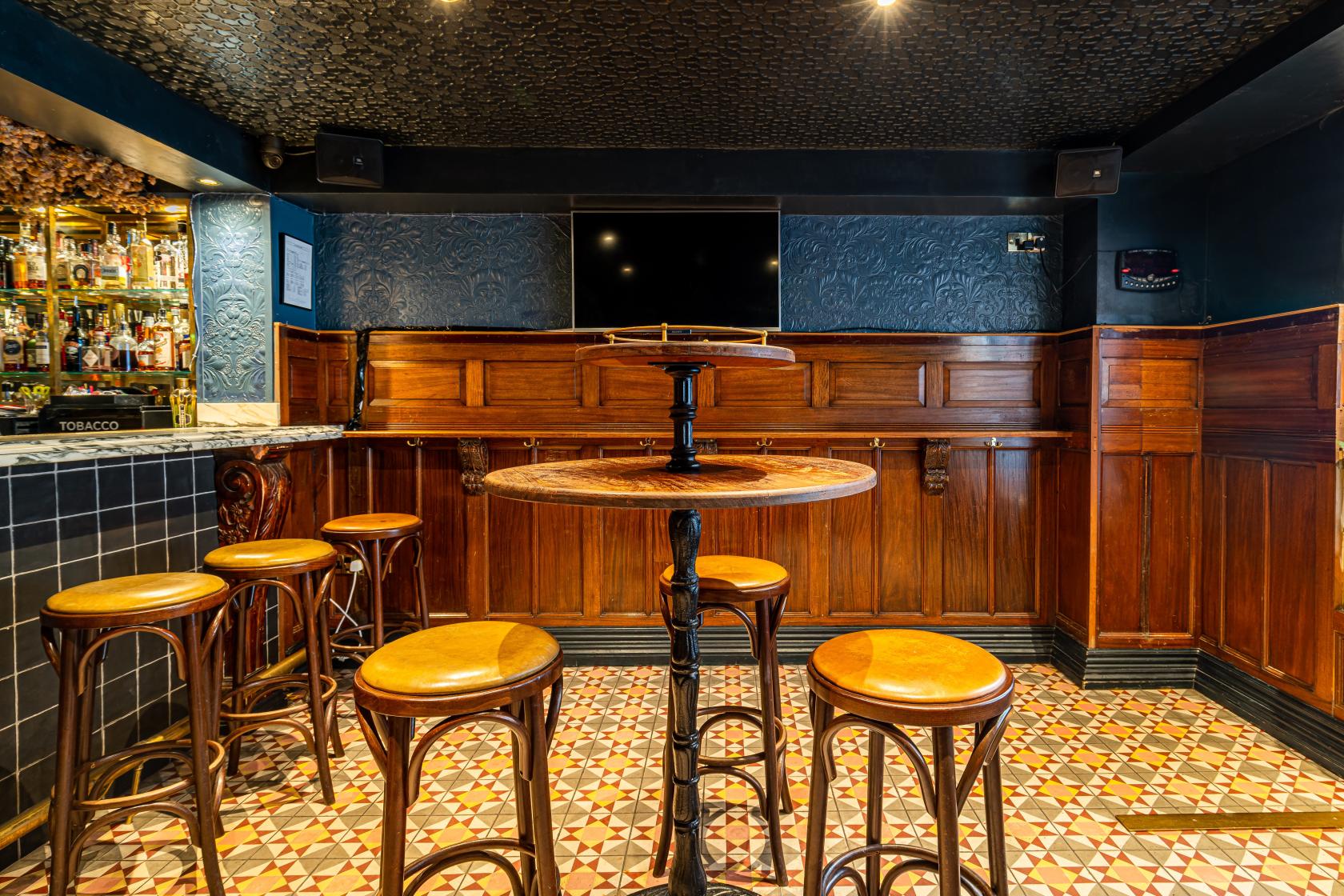 A pub interior with a round wooden high table, matching stools, patterned tile floor, and dark wood paneling at The Bay Horse Tavern.