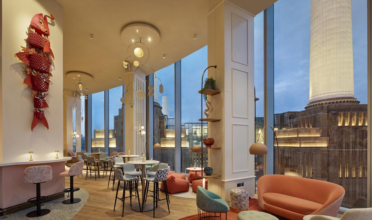 A hotel rooftop lounge with floor-to-ceiling windows, pastel seating, and city views at art'otel London Battersea Power Station.