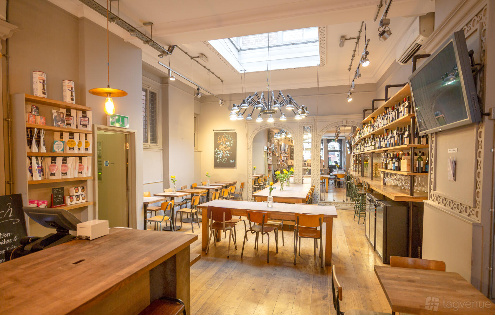 A cafe with wooden tables, a large skylight, and shelves stocked with bottles at Notes Coffee & Bars Trafalgar Square.