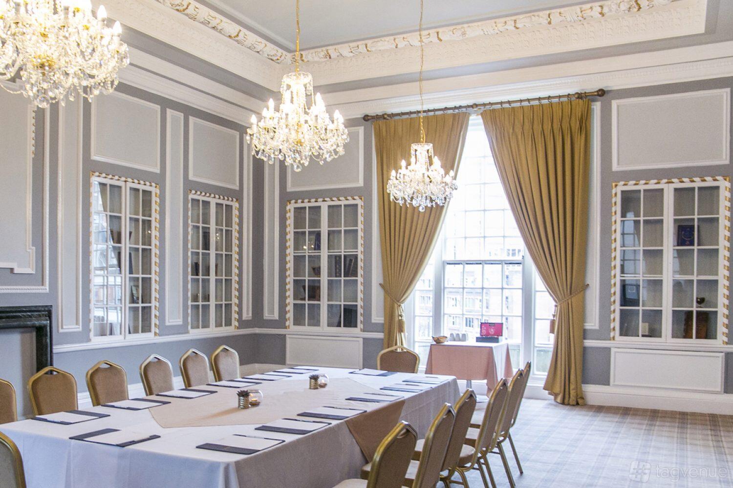 An event space with chandeliers, tall windows with gold curtains, and a boardroom setup at Manchester Hall.