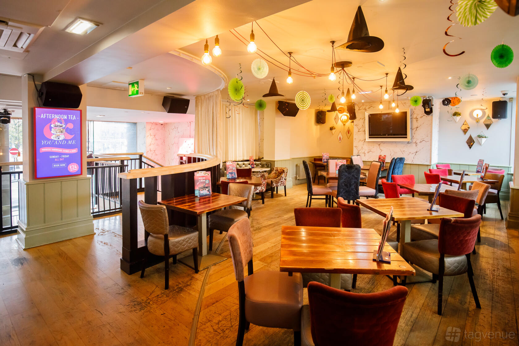 An event space in a cocktail bar with wooden floors, colorful chairs, hanging decorations, and large windows at Slug & Lettuce, Manchester Piccadilly.