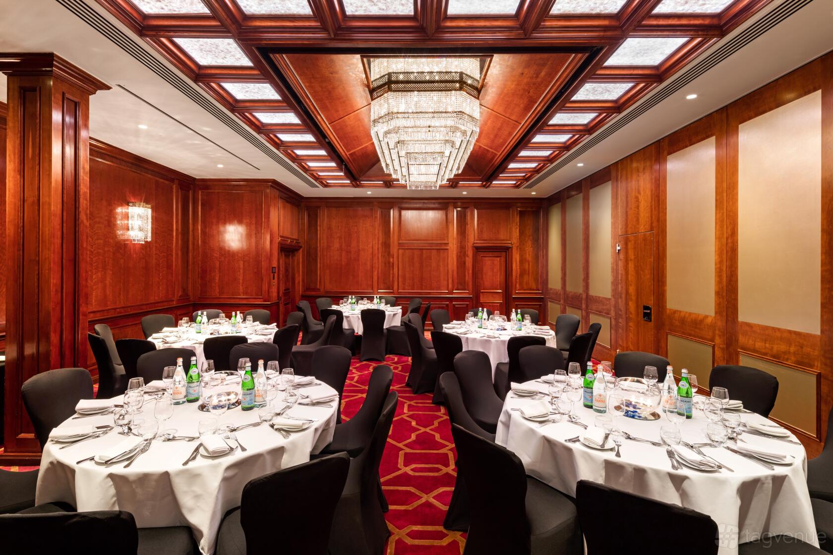 An event space with round tables, black chairs, wood paneling, and chandeliers at Radisson Blu Hotel, London Heathrow