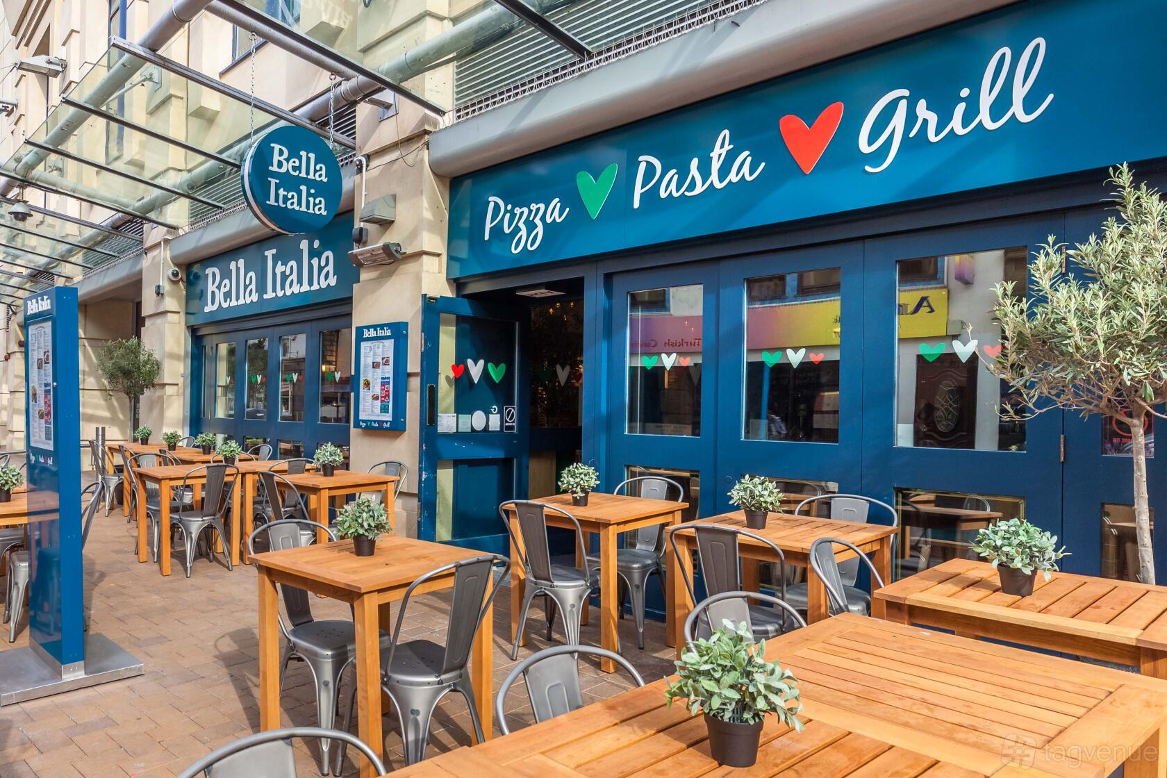 An outdoor restaurant seating area with wooden tables, metal chairs, and potted plants at Bella Italia - Nottingham Cornerhouse.