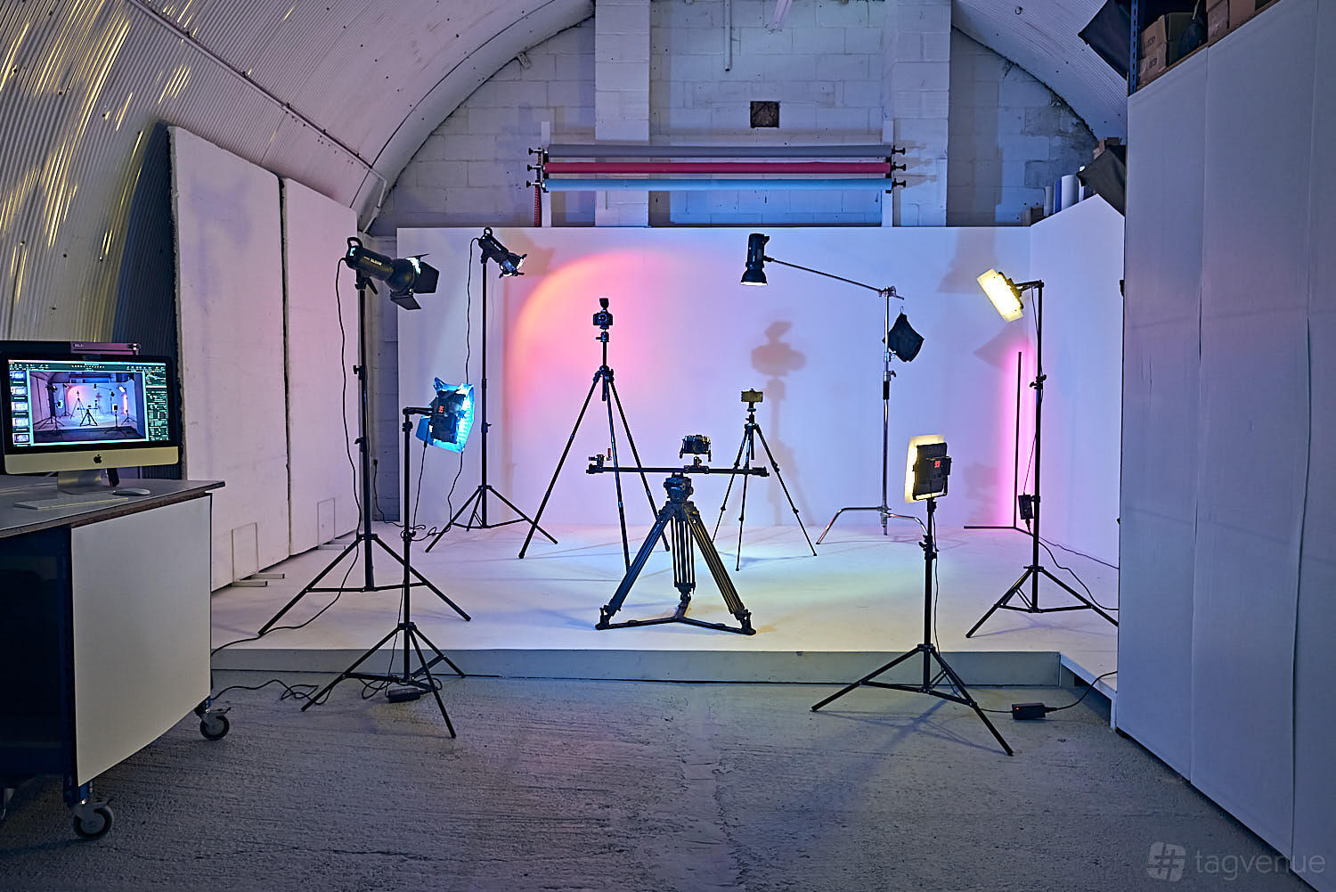 A photo studio with seamless white walls, adjustable colored lighting, and multiple professional cameras at Arch Photo Studio.