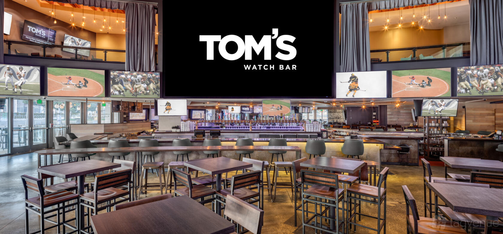 An event space with high-top tables, bar seating, and multiple large screens at Tom's Watch Bar Los Angeles.