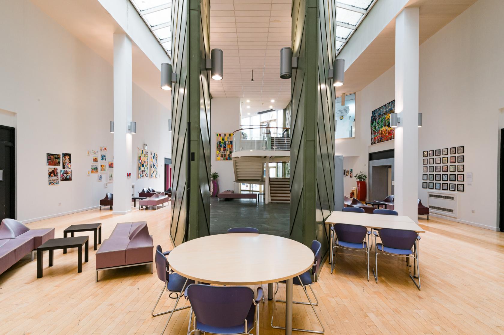 An event venue with round tables, purple chairs, high ceilings, artwork on white walls, and skylights at The Boardwalk.