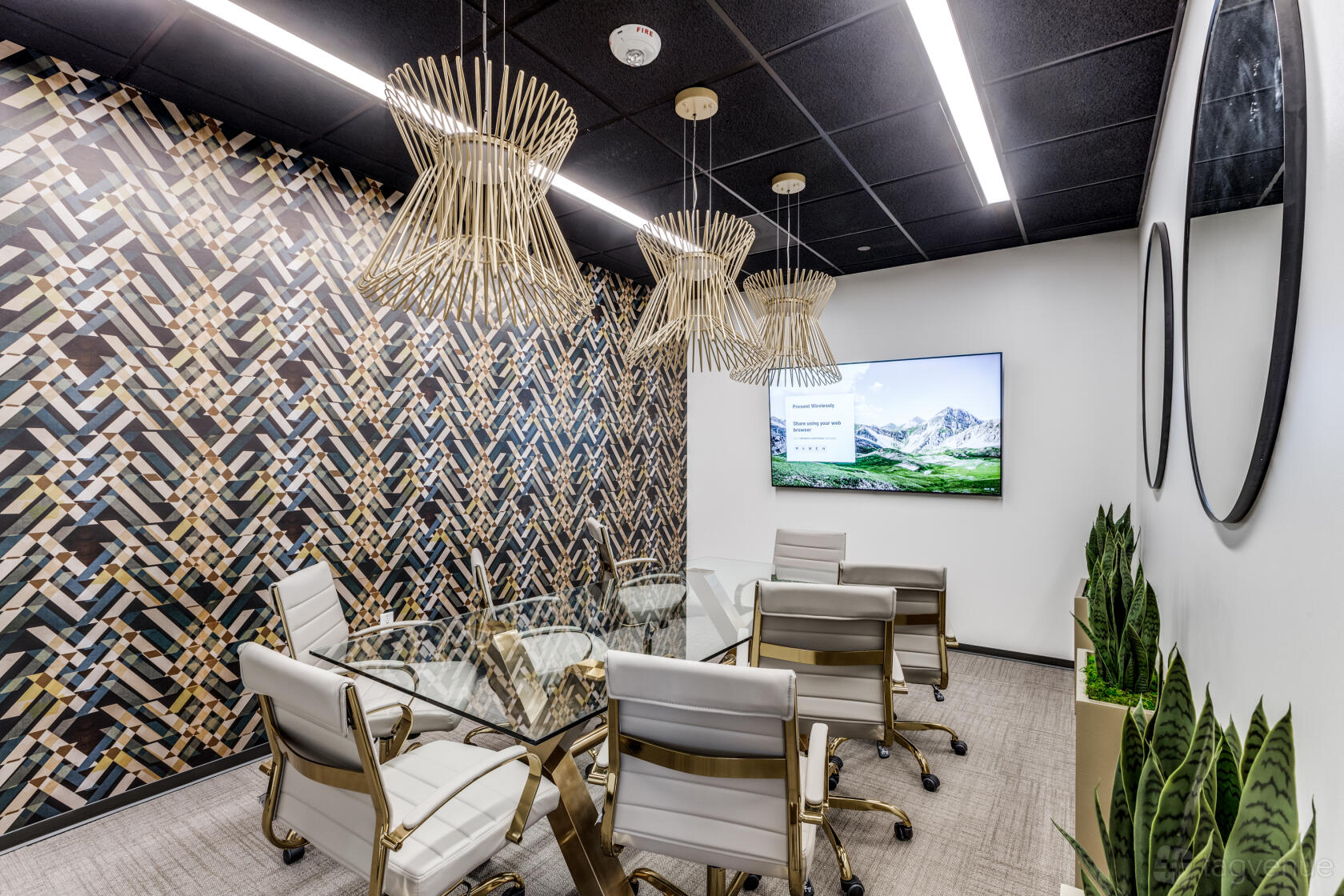 A boardroom with a geometric accent wall, glass table, gold pendant lights, and leather chairs at Lucid Private Offices - River Oaks / Greenway.