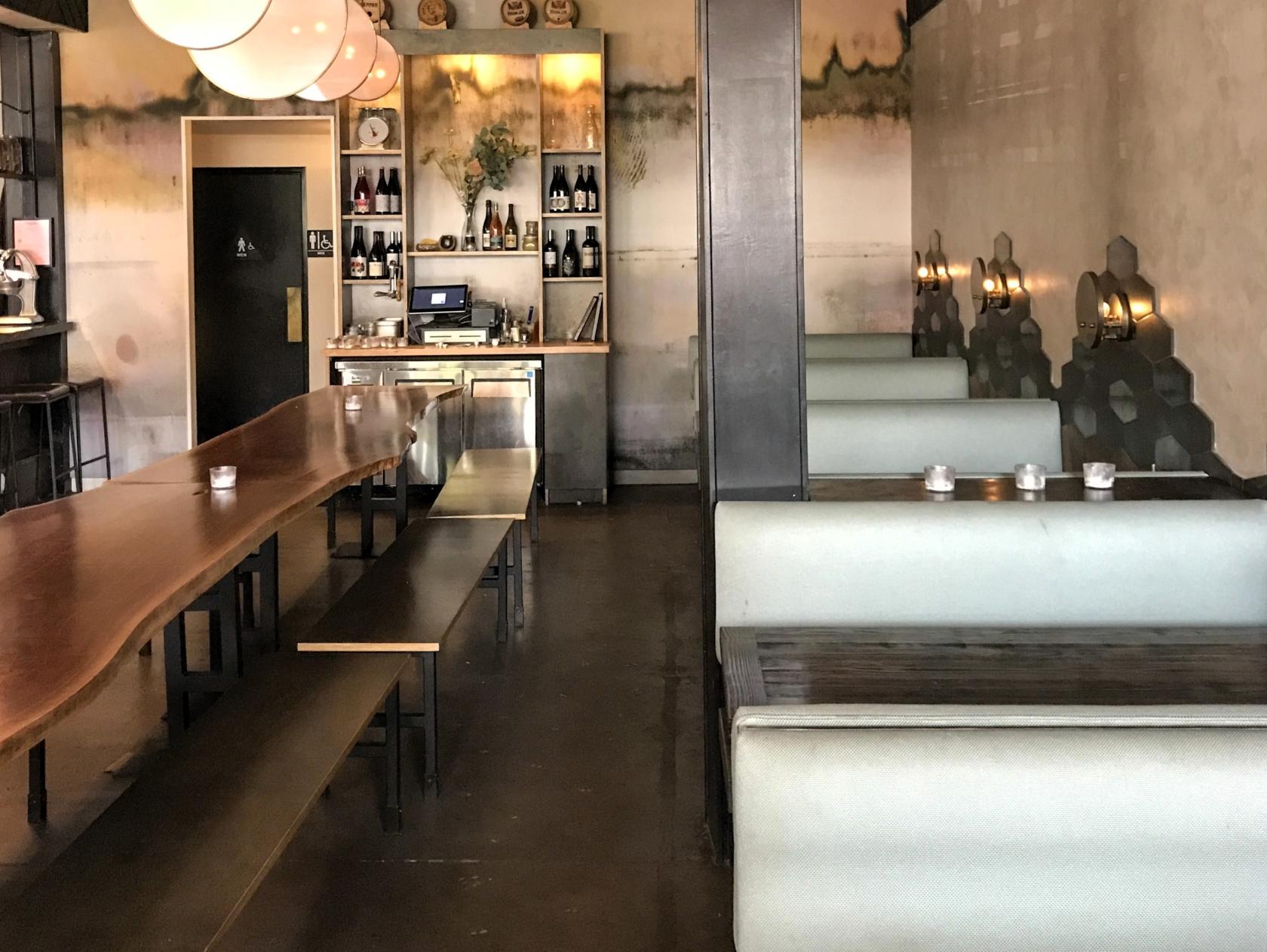 A restaurant with long wooden tables, bench seating, and pale booth seats along a textured wall at Ronan.