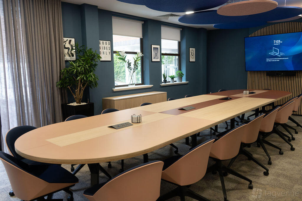 A meeting room with a long conference table, ergonomic chairs, wall-mounted screen, and large windows at Wizu Workspace - Leeds - 55 St Paul's.