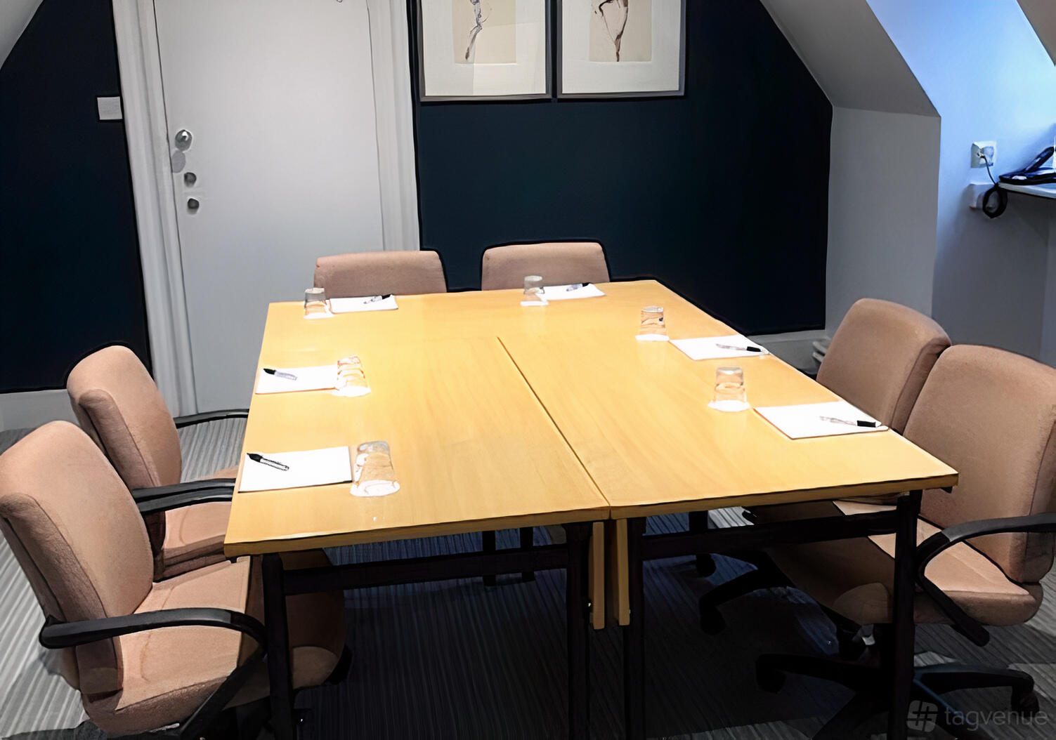 A meeting room with a rectangular wooden table, six upholstered chairs, notepads, and glasses at Barnett Hill Hotel.