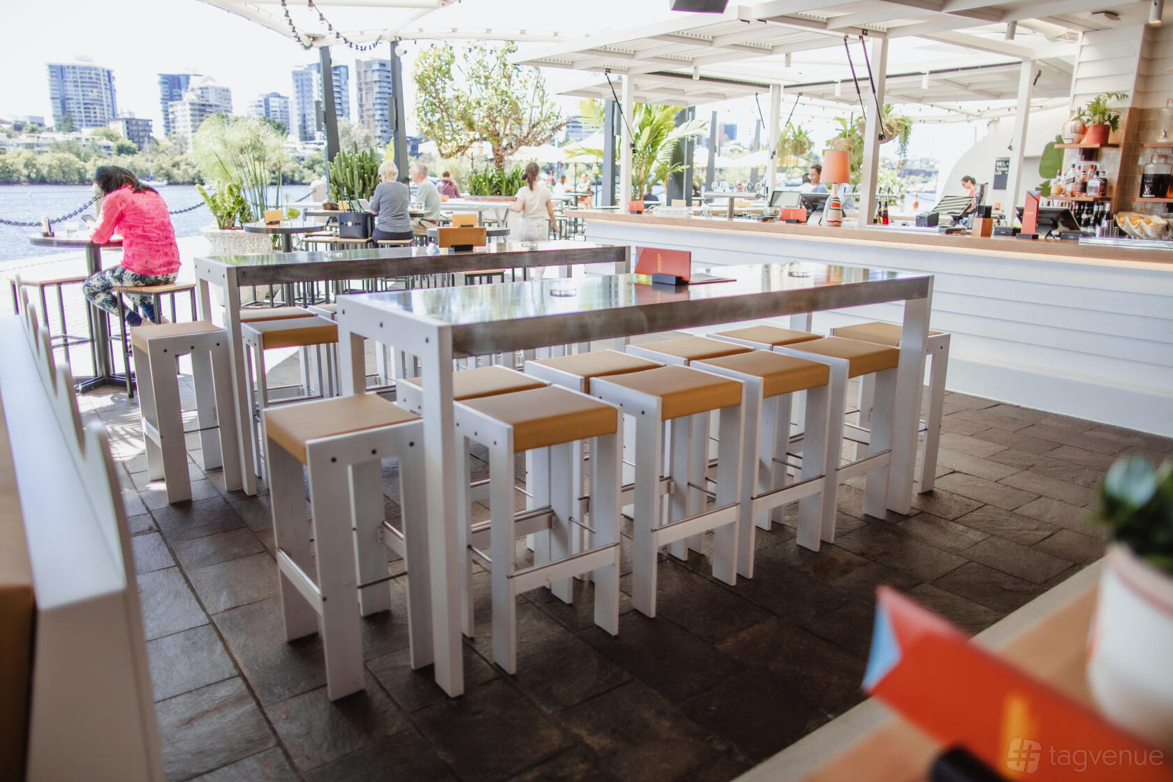 An outdoor bar space with high tables and stools, river views, and greenery at Riverbar & Kitchen.