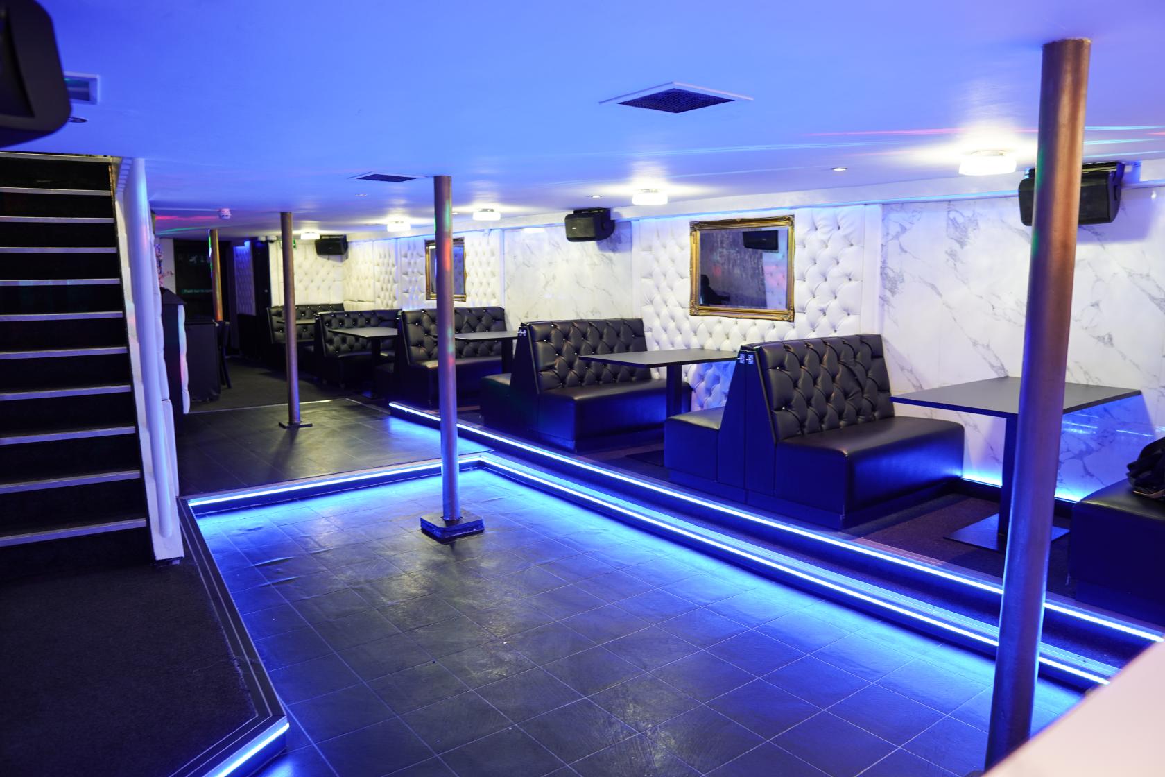 A nightclub bar with booth seating, tiled dance floor, and blue accent lighting at The Venue N10.