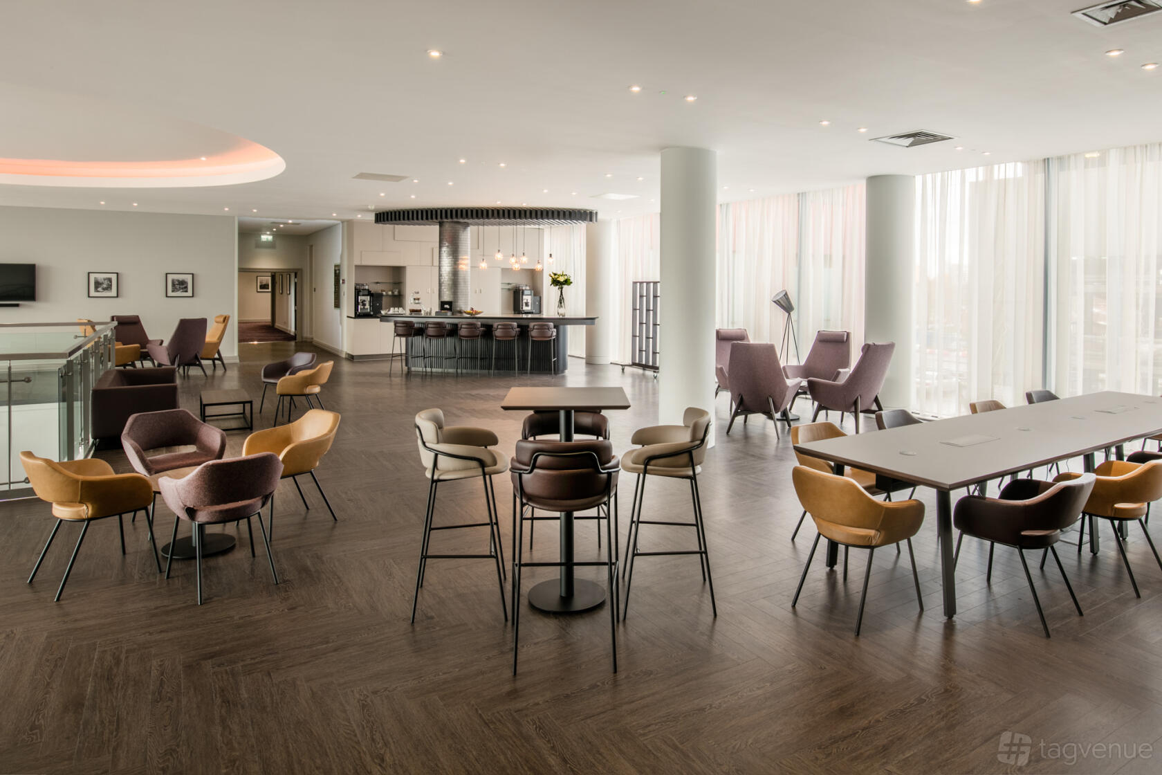 A lounge in a bar with floor-to-ceiling windows, modern armchairs, and communal tables at Crowne Plaza London Docklands.