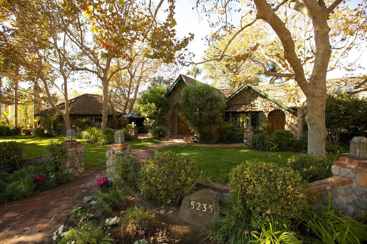 A stone cottage-style residence with a lush landscaped garden and shaded brick pathway at Enchanted Manor.