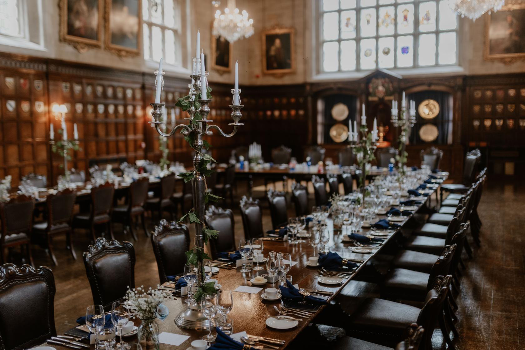 A historic hall with wood-paneled walls, chandeliers, long banquet tables, and candelabras at Ironmongers' Hall.