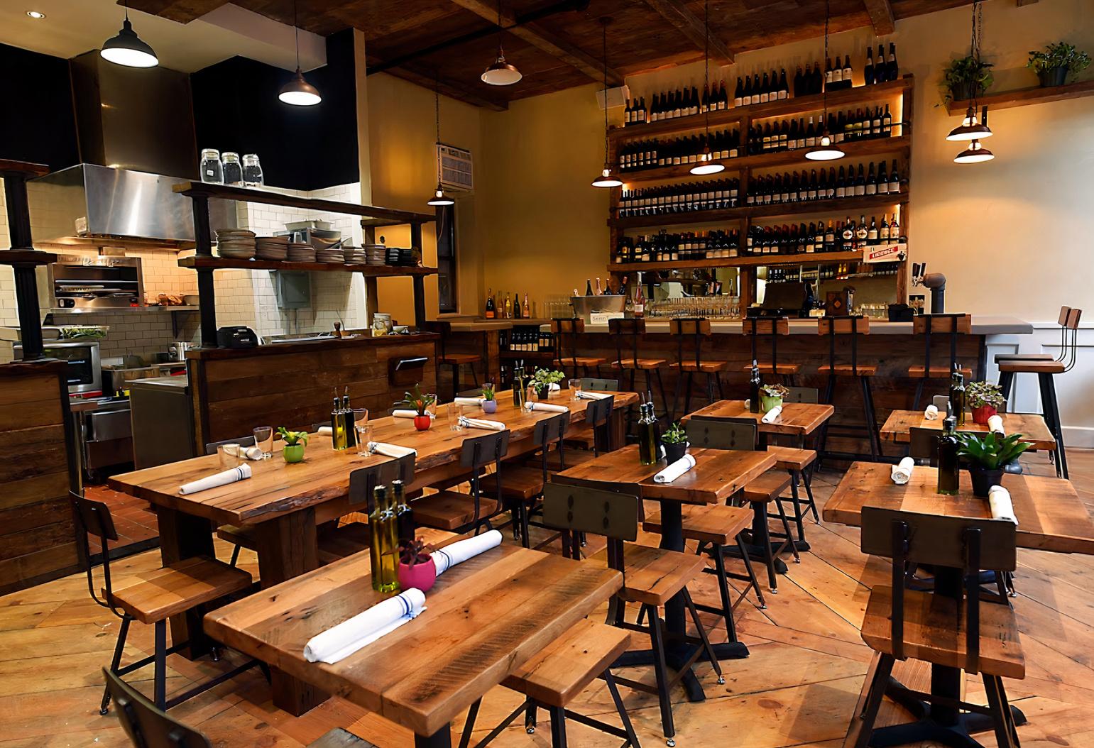 An event space in a restaurant with wooden tables, industrial chairs, and a wall of wine at St Tropez West Village.