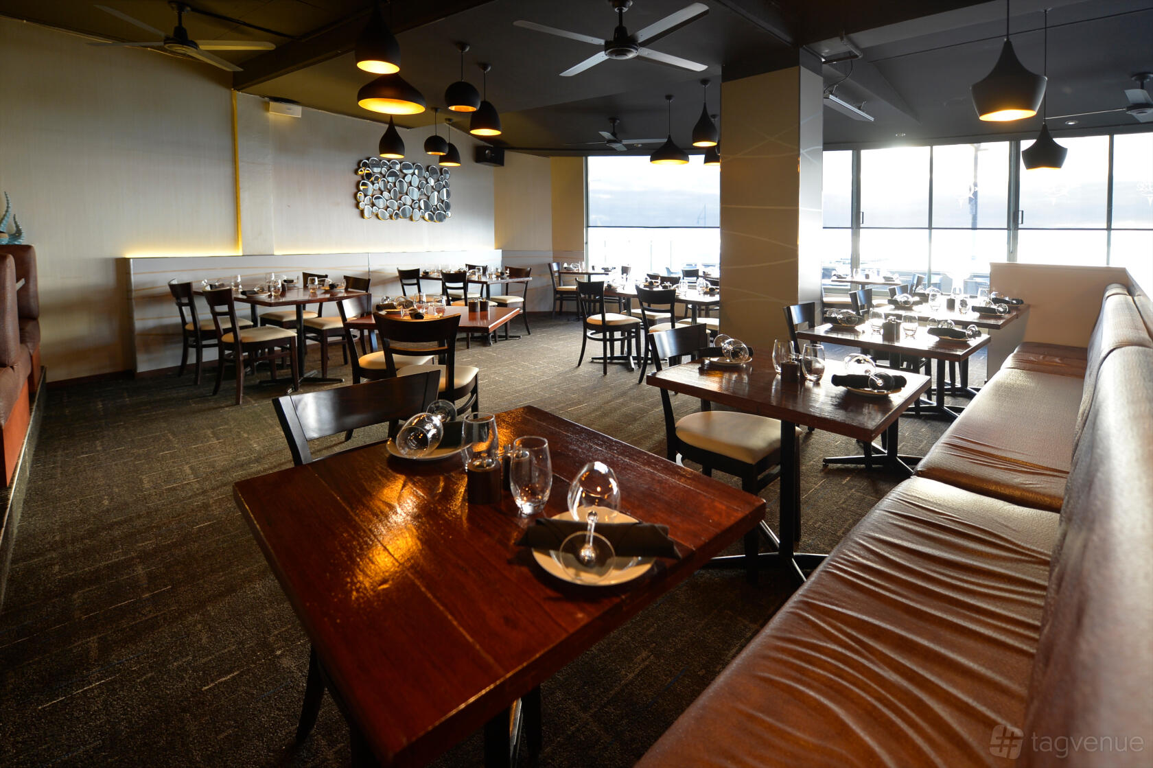 A restaurant dining room with wooden tables, cushioned bench seating, and large windows at Latitude 32.