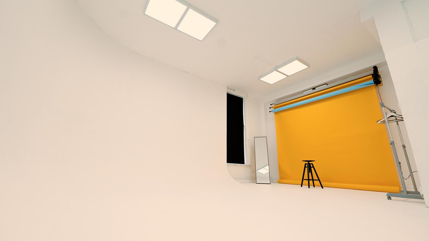 A photo studio with a curved white cyclorama wall, yellow backdrop, mirror, and black stool at Fade Street Studios.