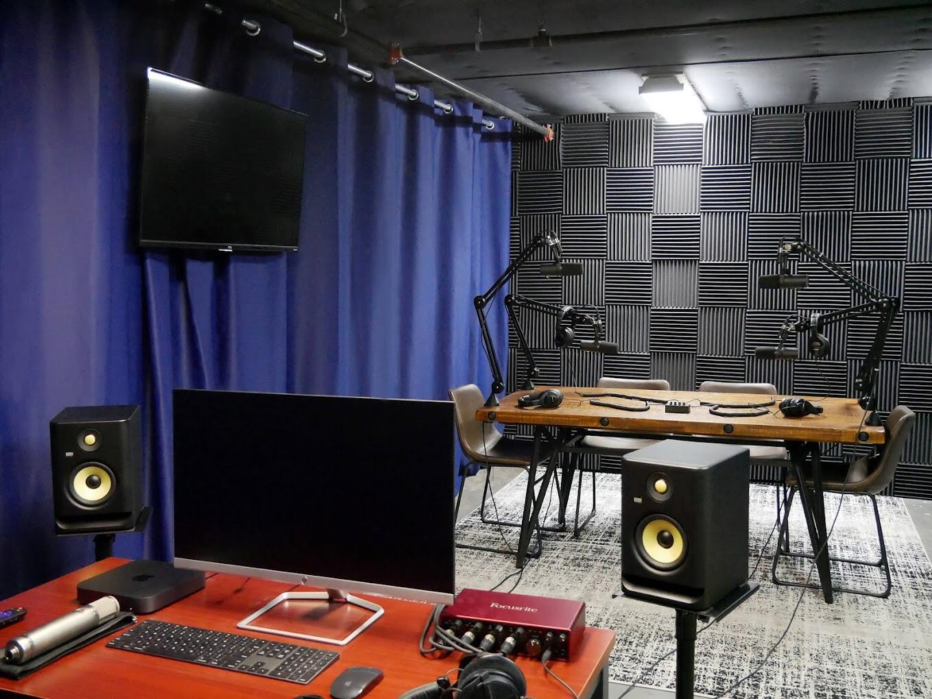 A podcast studio with soundproof foam panels, recording microphones, studio monitors, and a conference table at Pink Cloud Studios.