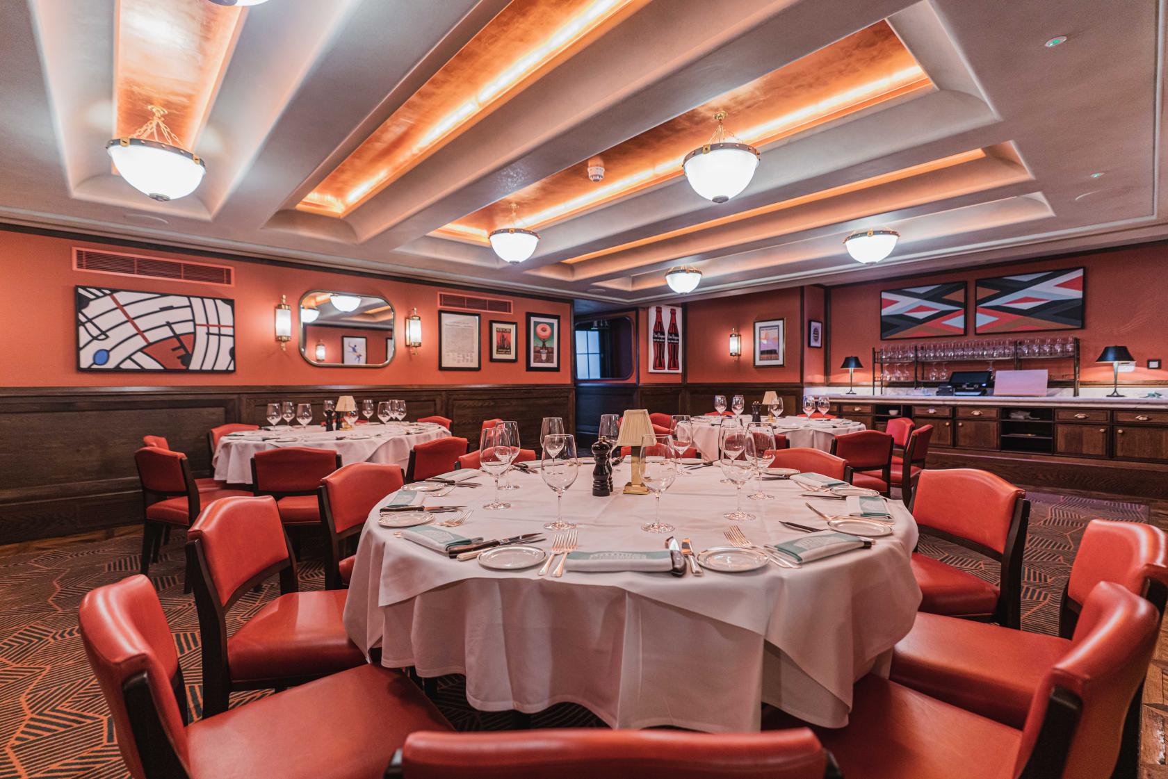 A dining room with round tables, red chairs, white linens, and wall art at Smith & Wollensky.