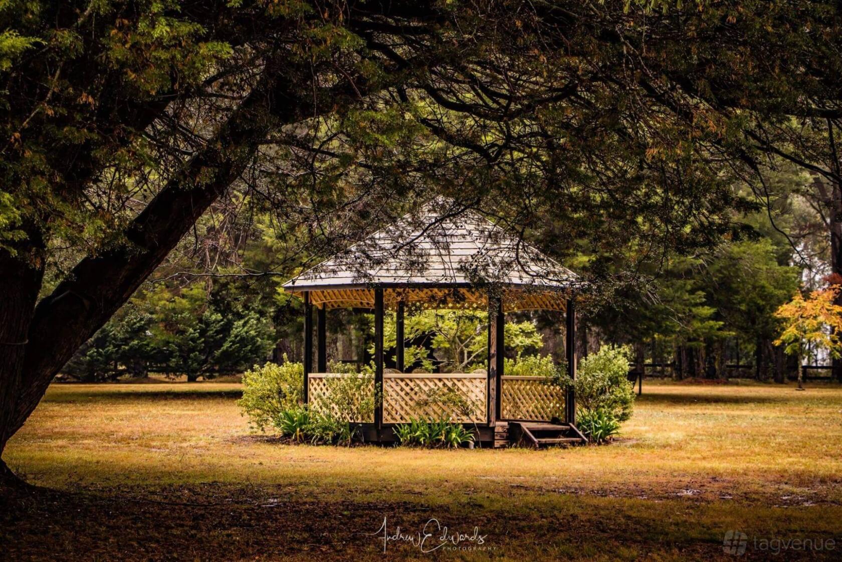 A barn venue with a wooden gazebo under large trees surrounded by grass at Sylvan Glen Estate.