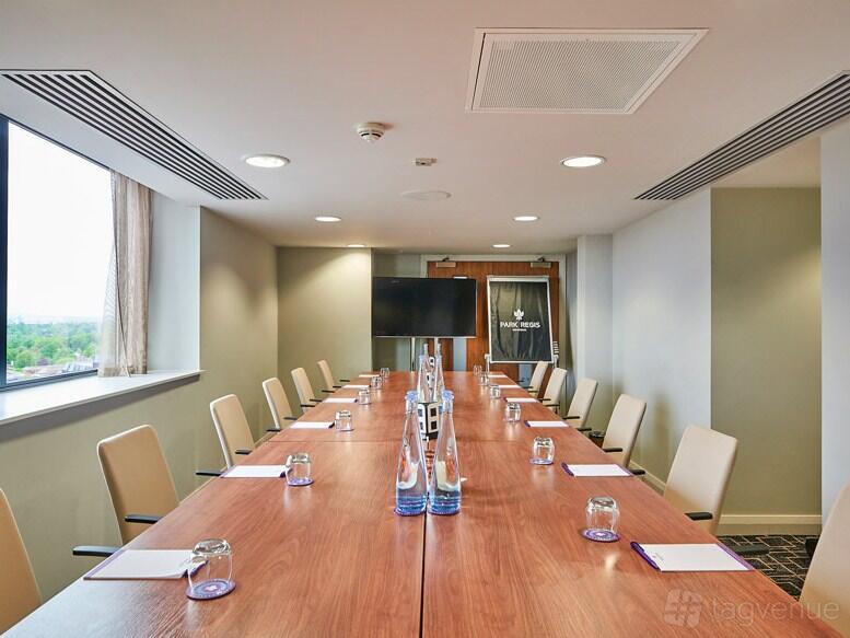 A hotel boardroom with a long wooden table, beige chairs, large windows, and a wall-mounted screen at Park Regis Hotel Birmingham.
