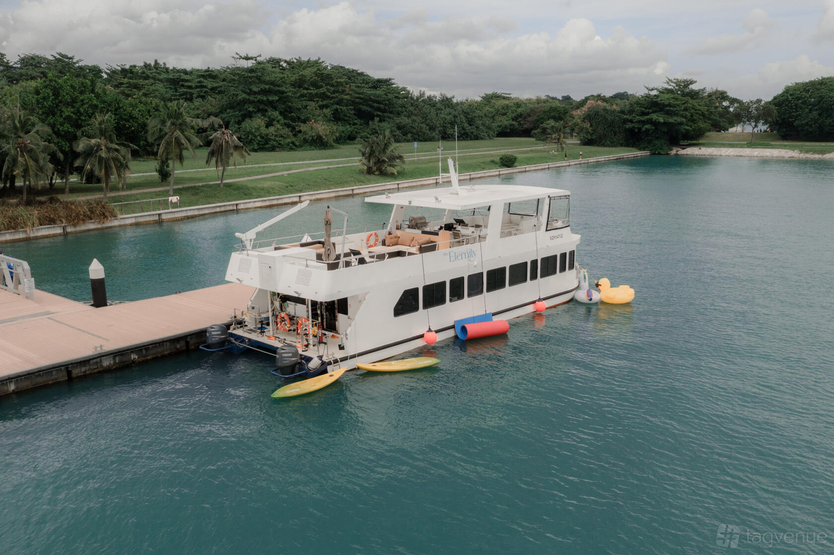 A white boat docked beside a pier with open-air seating and paddleboards on the water at MS Eternity.