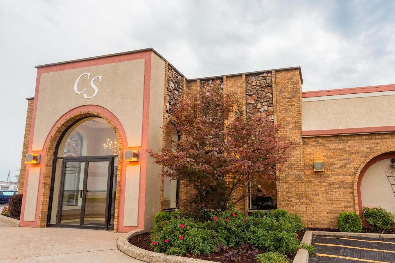 A banquet hall with large arched glass entry, stone and brick exterior, and landscaped shrubs at Crystal Banquets.