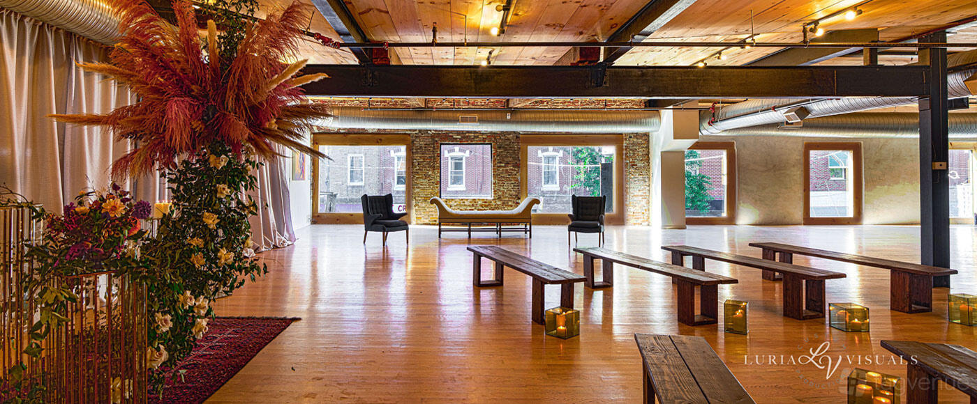 A loft with exposed brick walls, wood floors, large windows, and scattered benches at Loft On Passyunk.