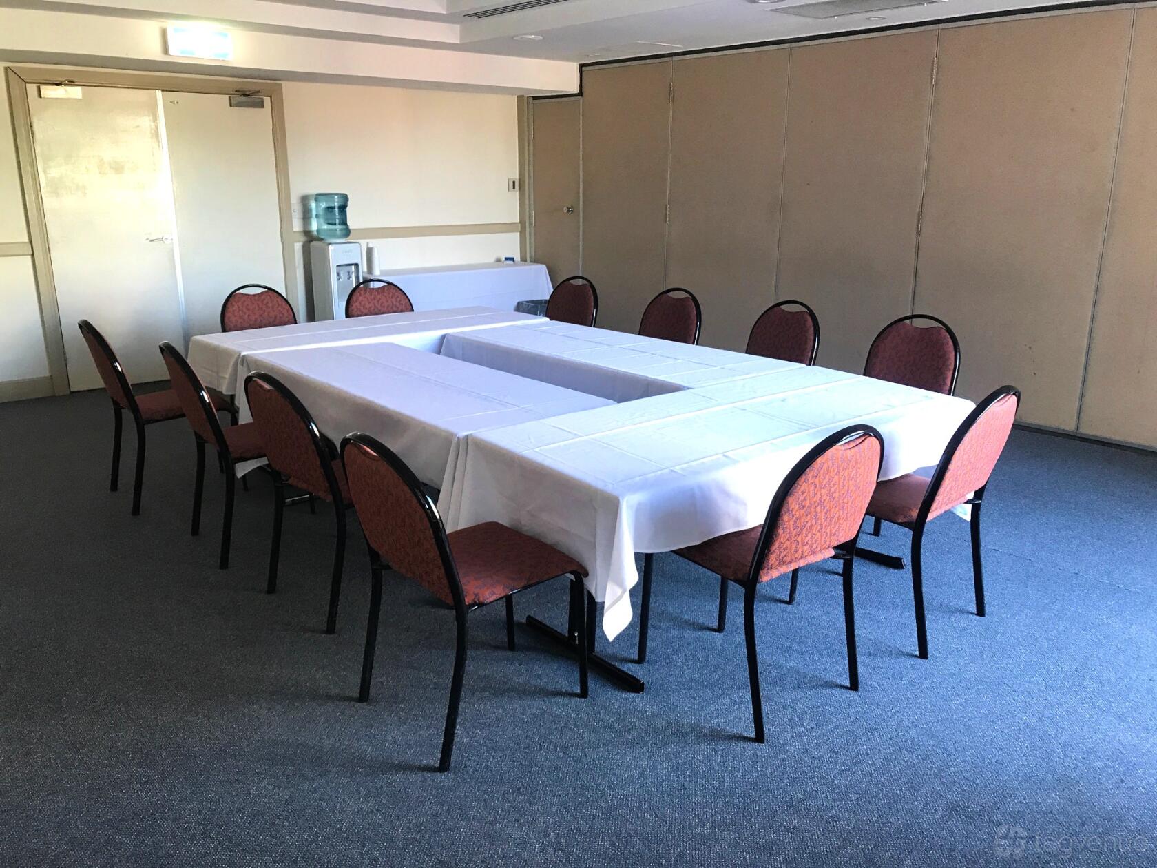 A meeting room with U-shaped tables covered in white linens and red cushioned chairs at Oaks Calypso Plaza.
