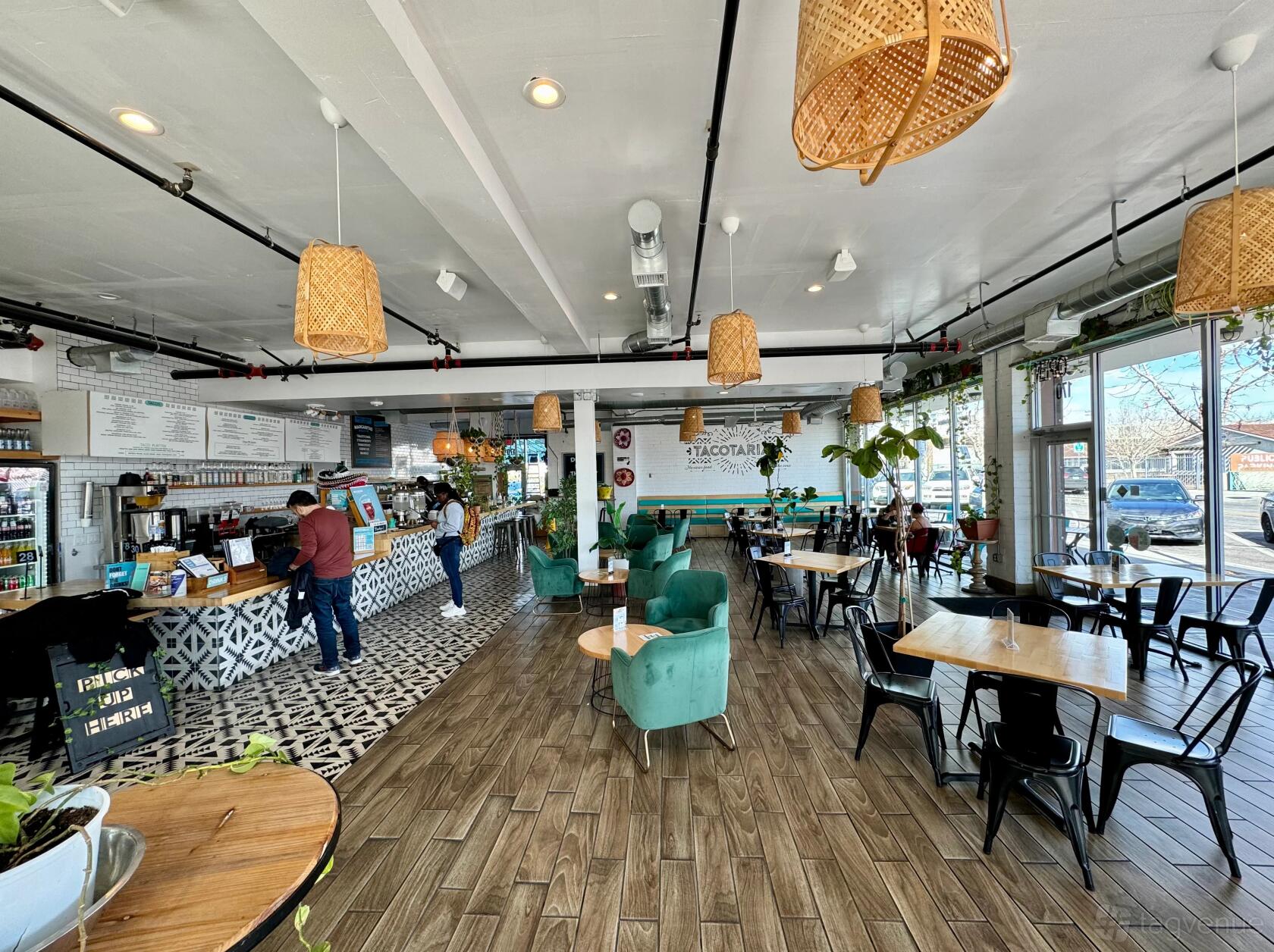 A restaurant with patterned tile flooring at the counter, teal armchairs, and hanging woven light fixtures at Tacotarian Downtown.