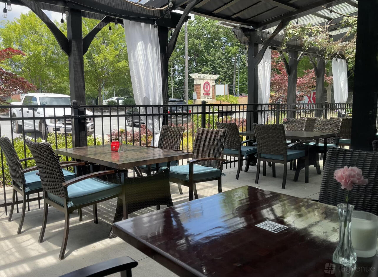 An outdoor patio with wicker chairs, wooden tables, and sheer white curtains at Colonial Kitchen and Bar.