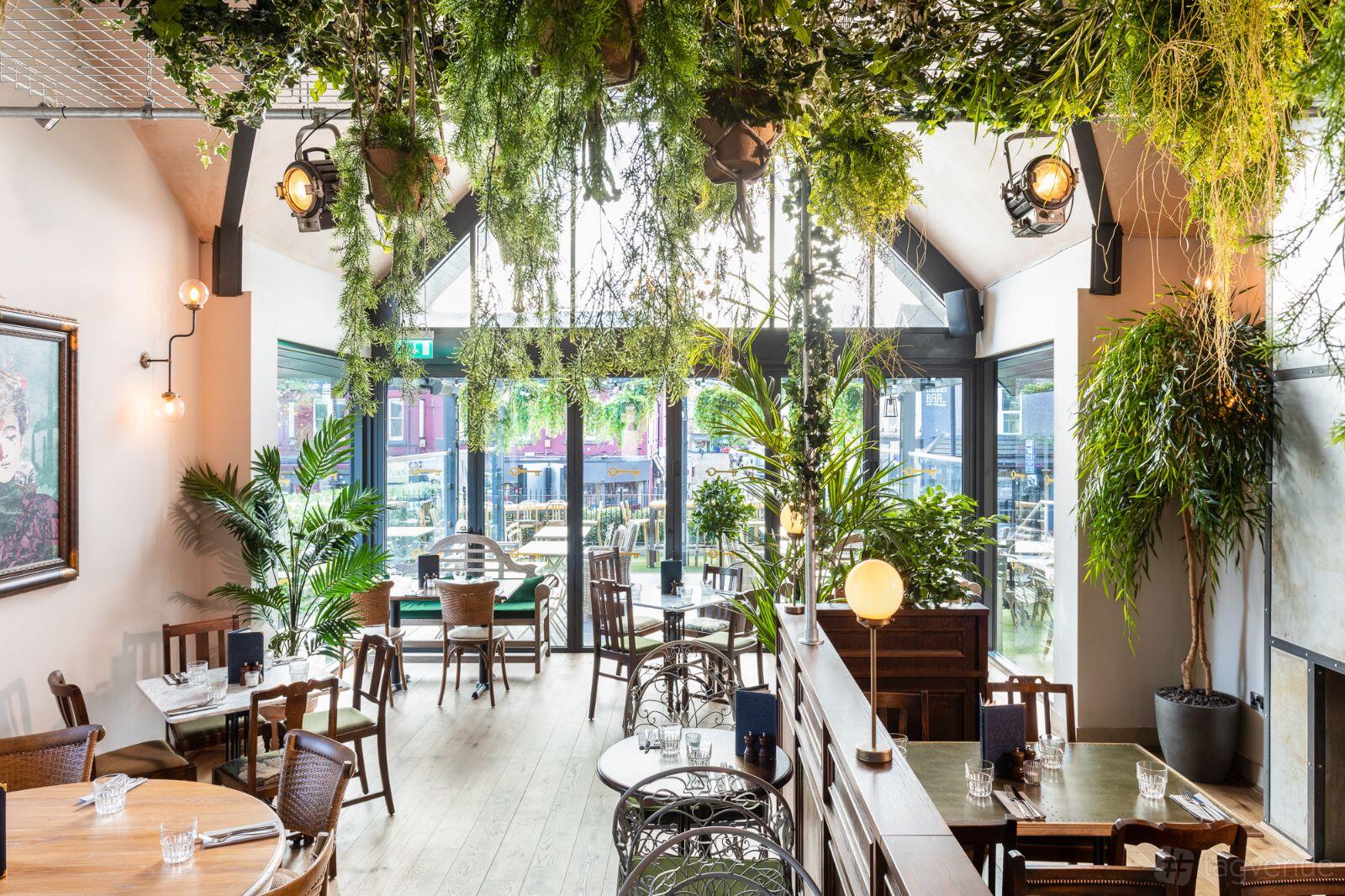 A bar restaurant with hanging greenery, skylights, and wooden tables at The Lost and Found Sheffield.