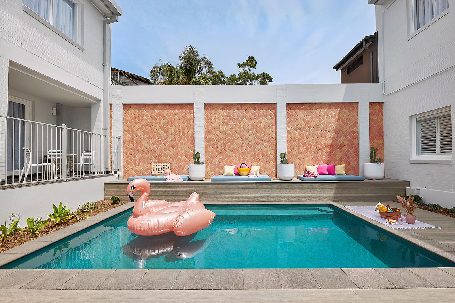 An outdoor hotel courtyard with a swimming pool, floating pink flamingo, lounge seating, and potted plants at The Courtyard, Adina Sydney Chippendale.