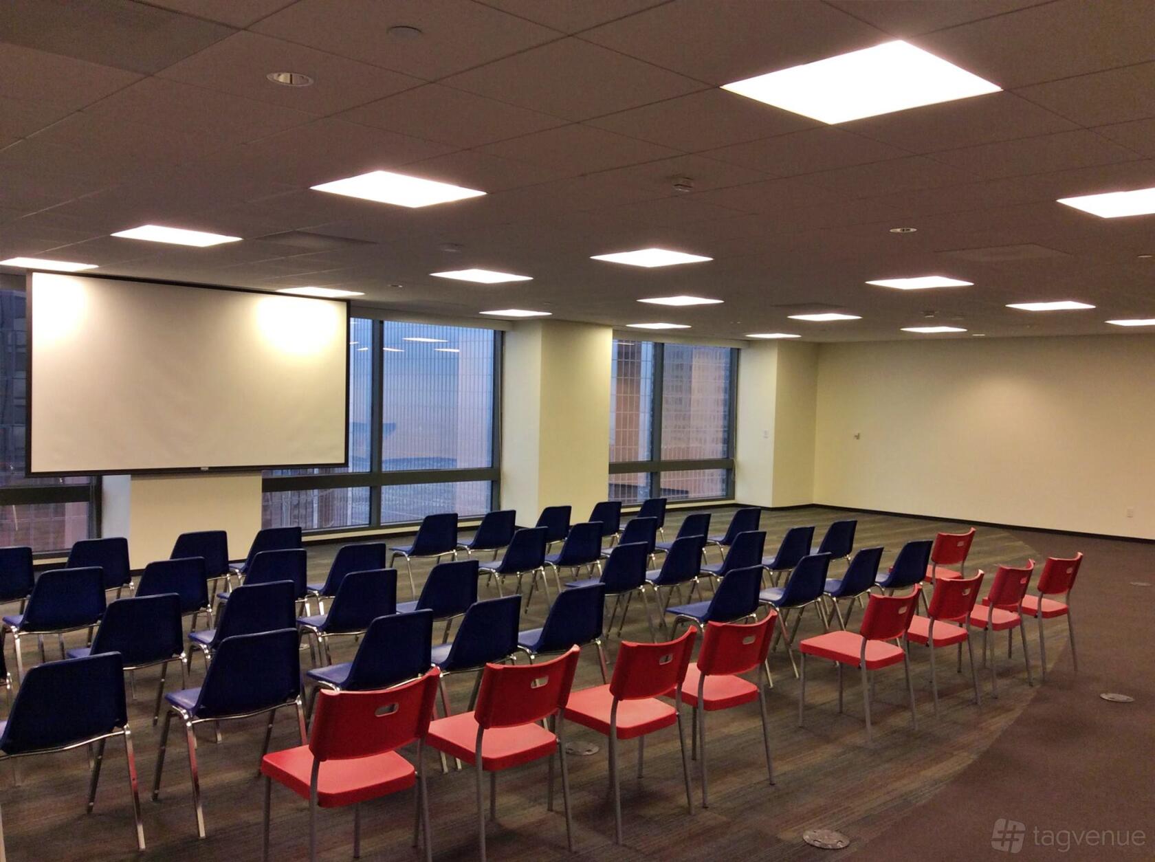 A conference hall with rows of colorful chairs, large windows, and a projector screen at Indie Desk.