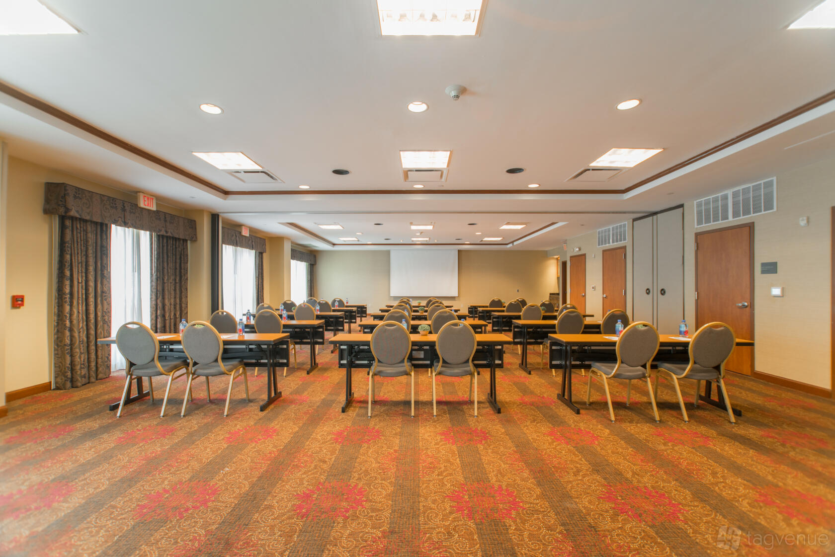 A ballroom with round-backed chairs, rectangular tables, and patterned carpet at Hilton Garden Inn The Woodlands.