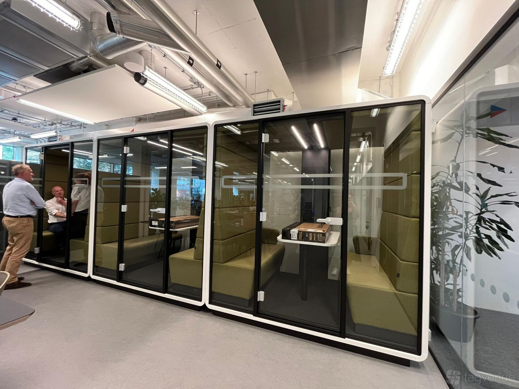 A glass-walled meeting pod with built-in seating and a central table at The Society Building - Fitzrovia.