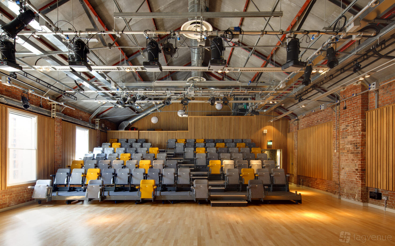A university theatre with tiered seating, exposed brick walls, and stage lighting at Collective Acting Studio.
