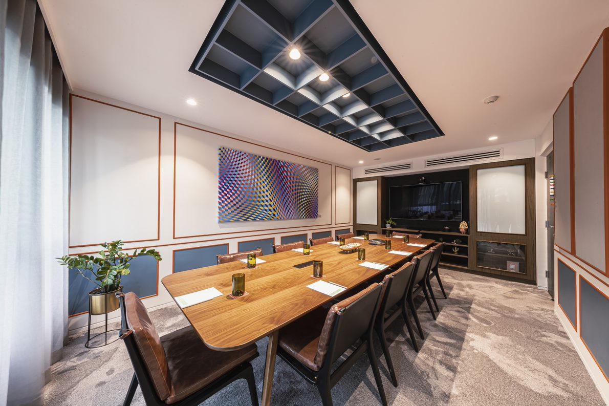 A boardroom with a long wooden table, leather chairs, modern art, and large windows at Ovolo The Valley.