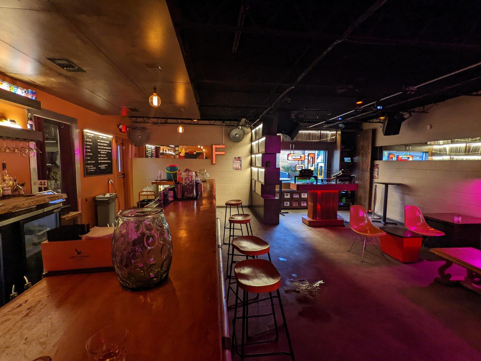 A bar with ambient neon lighting, high wooden counters, and translucent chairs at The Flat Houston.