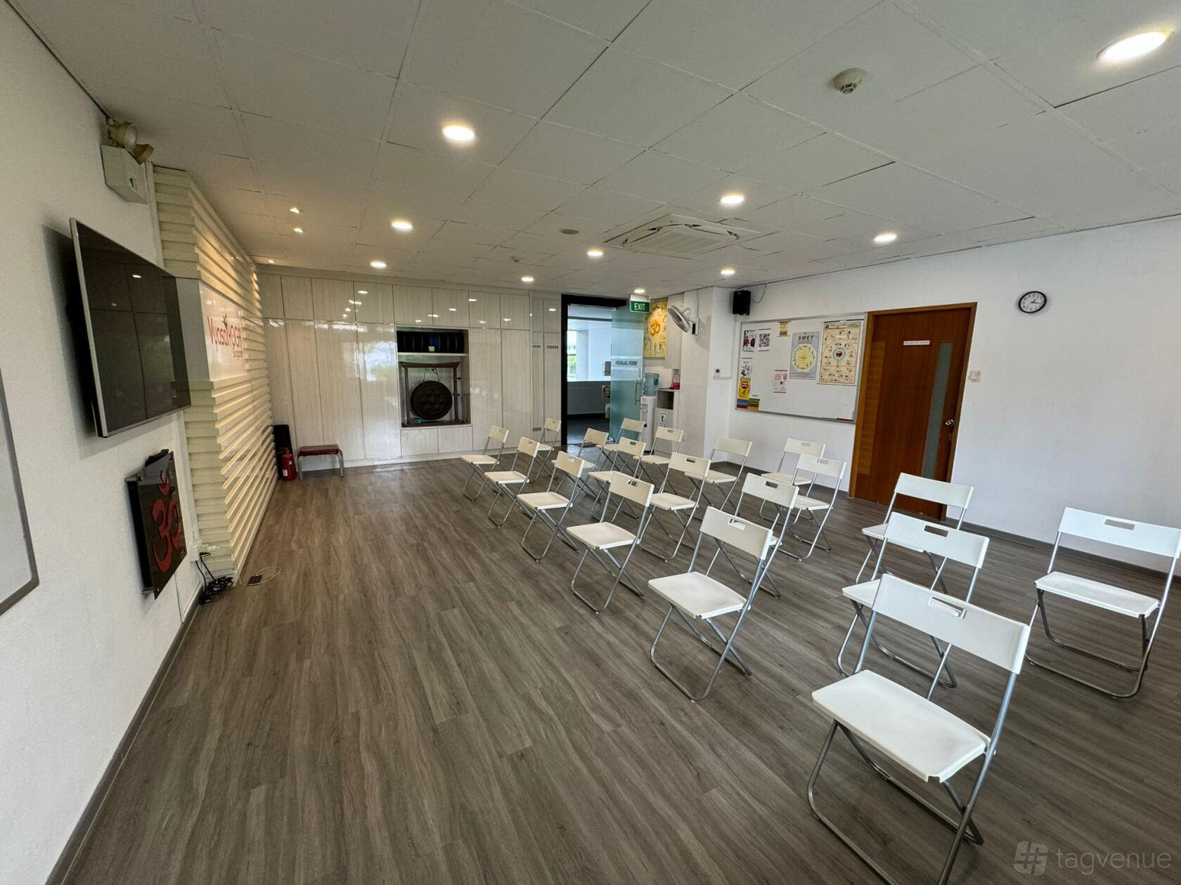 A yoga studio with folding chairs arranged in rows, wood flooring, and wall-mounted screens at Vyasa Yoga Singapore.