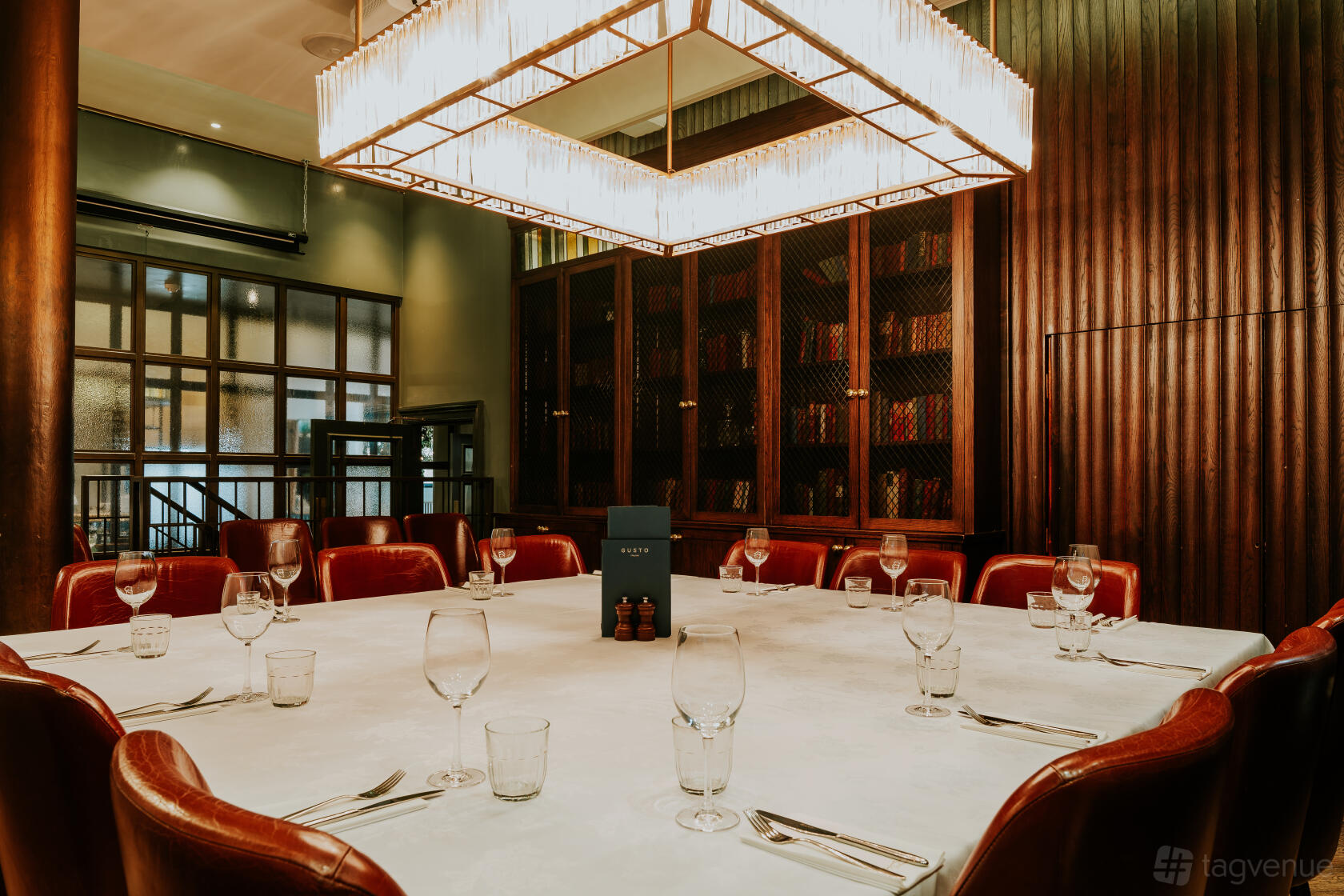 A dining room with a large round table, leather chairs, and a chandelier at Gusto Italian Manchester.