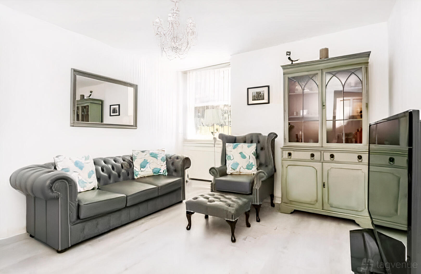 An apartment living area with a tufted gray sofa, wingback chair, vintage cabinet, and chandelier at Blackheath Flat for Photos, Filming & Events.